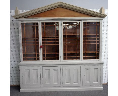 A grey painted bookcase cabinet, with architectural cornice fitted with novelty chimney pots over four glazed doors and four 