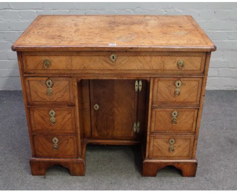 A Queen Anne walnut veneered chequer banded kneehole desk, the moulded edge quarter veneered crossbanded top above a fitted l