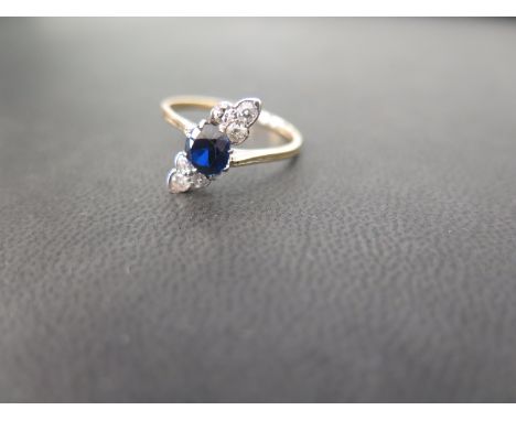 A sapphire and diamond crossover dress ring - The circular-shape sapphire to the trefoils of vari-cut diamonds - Stamped 18ct