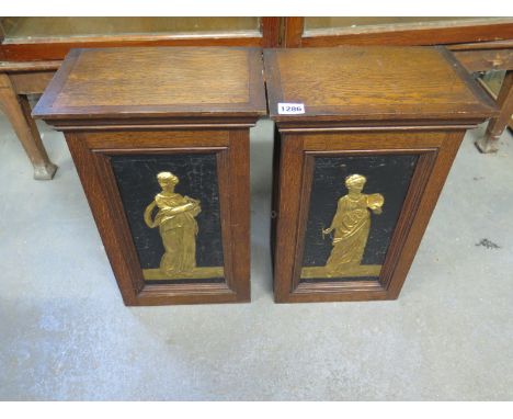 A pair of Arts and Crafts oak cabinets each having a single shelf and a lockable door decorated in gilt with a classical figu