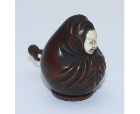 A Japanese carved boxwood netsuke depicting a seated figure, with ivory face and removable base enclosing small storage compa