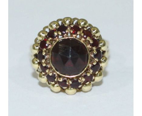 A 14ct gold dress ring set with a large central round faceted amethyst ring and further surrounded by fourteen small garnets,