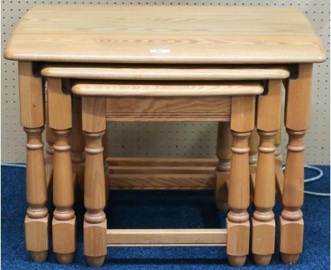 A contemporary Ercol elm nest of three tables with shaped tops on turned supports joined by stretchers, 44cm high x 62cm wide