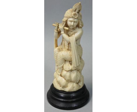 An early 20th century Indian ivory figurine, carved to depict a lady playing a flute, mounted on an ebonised plinth, height 1