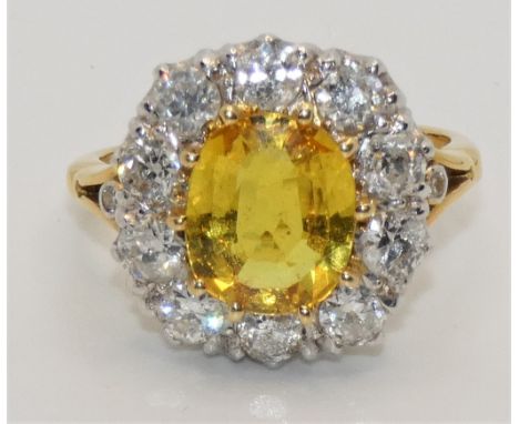 An 18 ct gold yellow sapphire and diamond cluster ring, claw set with an oval mixed cut stone, measuring 10 x 8.4 x 3.9 mm, c