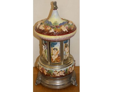 A polychrome porcelain and electroplate cigarette dispenser carousel, decorated with raised Cherubs playing musical instrumen