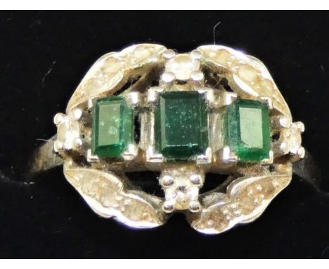 An 18ct gold emerald and diamond dress stone ring, claw set with three emerald cut stones, bordered by rose and brilliant cut