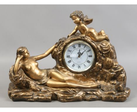 A gilt painted composite mantle clock with semi naked female and cherub over quartz timepiece raised on a naturalistic base.
