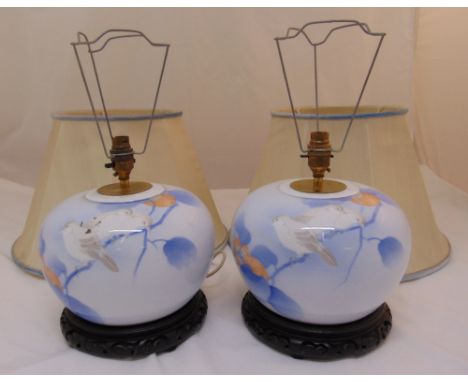 A pair of ceramic table lamps, bombe form decorated with birds on branches with detachable silk shades and carved hardwood st