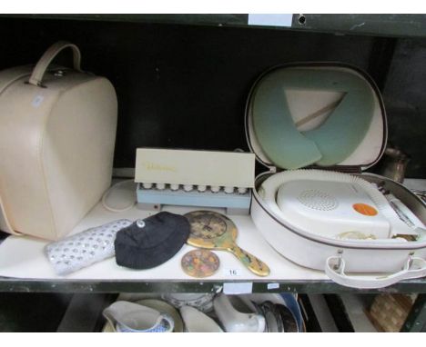 A shelf of vanity items including hair dryer, electric curlers, vanity case etc