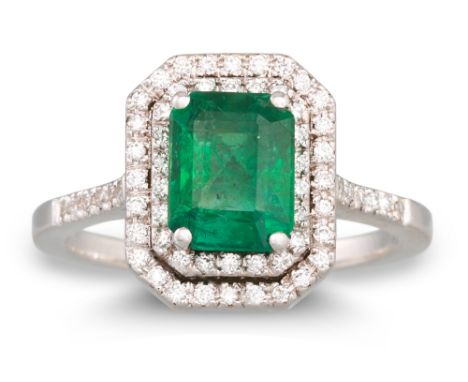 AN EMERALD AND DIAMOND CLUSTER RING, the trap cut emerald to a two rowed diamond surround, diamond shoulders, mounted in 18ct