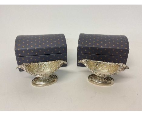 Pair of silver boat shaped salts with embossed decoration, in domed cardboard trunk-type boxes, with one spoon