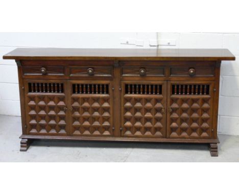 A Spanish-style mahogany sideboard, four drawers over four carved cupboard doors with inset carved panels on stepped bracket 