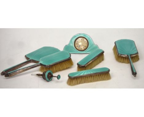 A George V seven-piece enamelled dressing table set, comprising eight-day clock, two hand brushes, two further brushes, a han