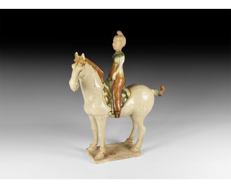 An undated archaistic glazed ceramic horse and rider figurine on a rectangular base with green and brown glaze detailing; rid