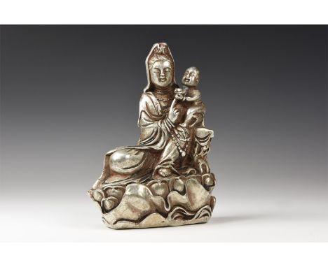 An undated archaistic silver-coloured metal figure of the goddess Kwan Yin seated on a large lotus flower in long flowing rob
