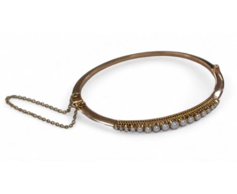 A late Victorian natural half pearl yellow metal bangle, with seventeen graduated pearls, largest 4mm diameter, on a yellow m
