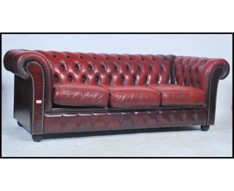 A ox blood leather low back three - seater Chesterfield sofa, with deep button back and sides, scrolled arm rests and brass s