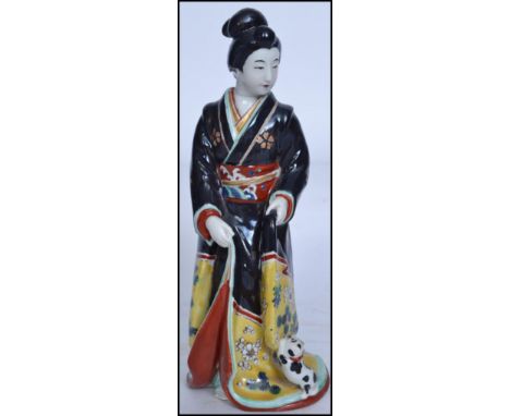 An early 20th century Oriental ceramic porcelain figurine of a Japanese Geisha Girl being hand painted with black gown having