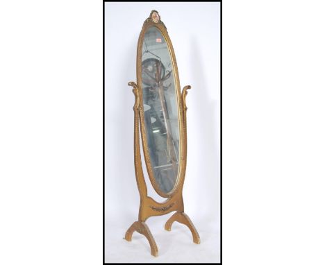 A 1950's mid century gilt rococo cheval mirror having an elongated oval swing mirror being raised on shaped supports all with