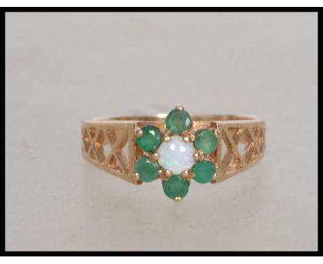 A hallmarked 9ct gold ring set with  a central opal stone surrounded by an emerald halo. Hallmarked London. Weight 2.8g.  Siz