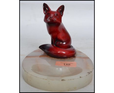 An early 20th century Royal Doulton ceramic flambe fox in a seated position in the famous flambe red glaze mounted on an onyx