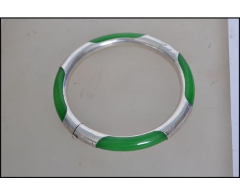 A vibrant green jade bangle held in a 925 silver bangle etched with light detailing having a snap clasp.