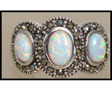 A silver ladies Art Deco style 3 stone opal ring. Each stone of cabochon form having marcasite concentric halo's. Weight 6.1g