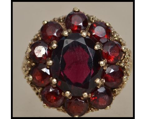 A hallmarked 9ct gold and garnet 1970s cluster ring having pierced and textured gallery and shoulders. Size R. Total weight 8