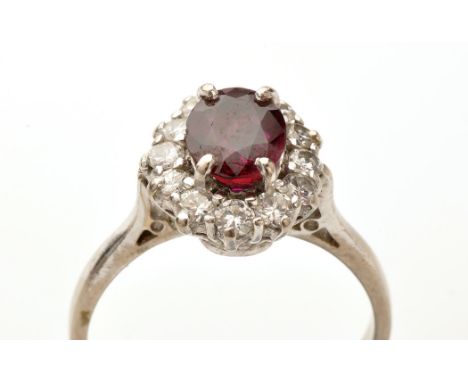 A ruby and diamond cluster ring, the oval facet cut ruby four claw set surrounded by twelve brilliant cut diamonds in a cage 