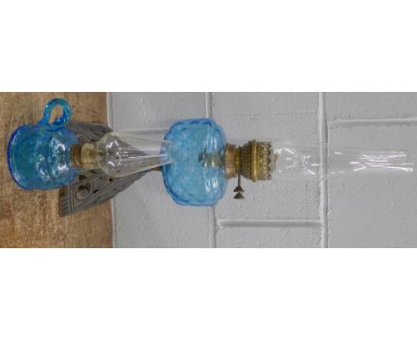 An oil lamp with pale blue glass reservoir on a cast metal base and a smaller oil lamp with blue glass reservoir