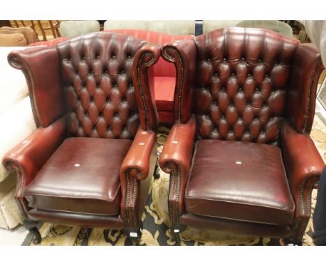 A pair of modern red leather upholstered wing back armchairs with button backs and scroll arms raised on cabriole legs