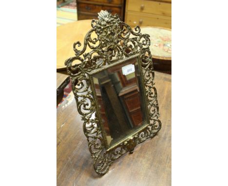A lacquered brass framed easel mirror with mask and scrolling foliate decoration in teh Rococo style