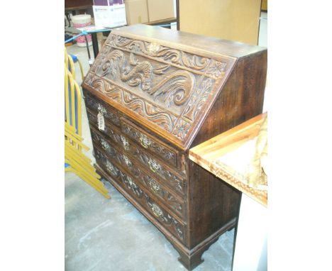 A 19th century oak bureau , the fall front carved with a scrolling leaf frieze and centred with a scaly sea serpent enclosing
