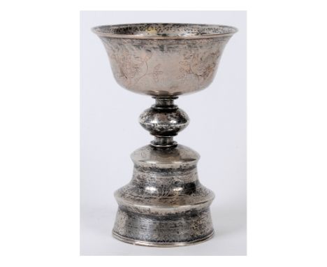 A Tibetan silver coloured metal stem cup or butter lamp, the flaring body raised on a tall knopped foot, engraved flowers and