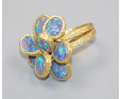 A 1970's? textured 18ct gold and eight stone oval black opal set dress ring, size K/L.