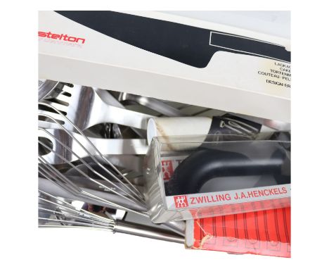 A large group of stainless steel kitchen utensils, including a boxed Stelton cake slice, a boxed Zwilling knife sharpener, bo