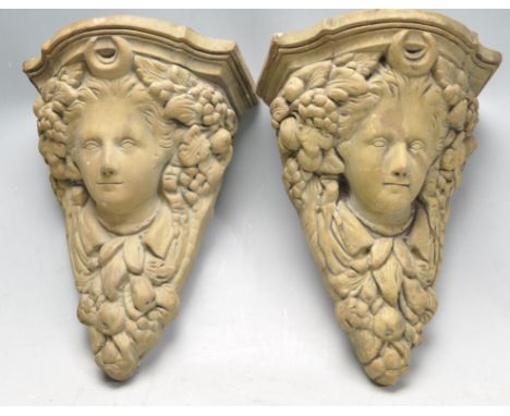 A pair of vintage 20th century classical style composite stone corbels having a pediment top over a cherubs face decorated wi
