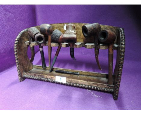 A tobacco smokers pipe rack and selection of pipes including HM silver rimmed