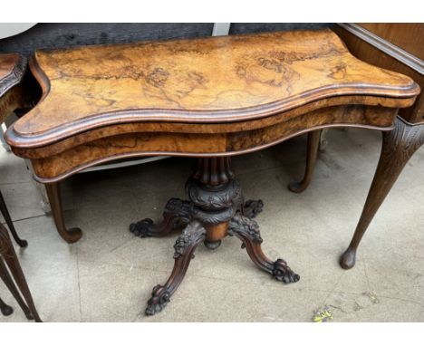A Victorian burr walnut card table, with a serpentine fold over top enclosing a baize interior on a carved column base and fo