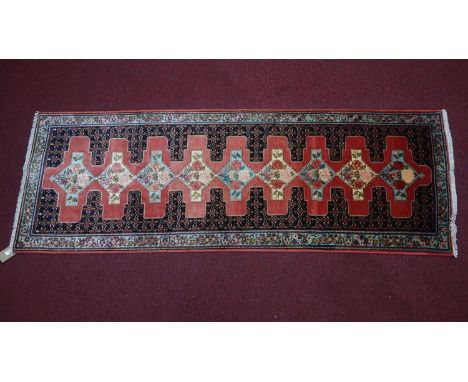 A Northwest Persian Senneh runner, repeating stylised diamond shaped medallion with repeating Heratie motifs on a rouge field
