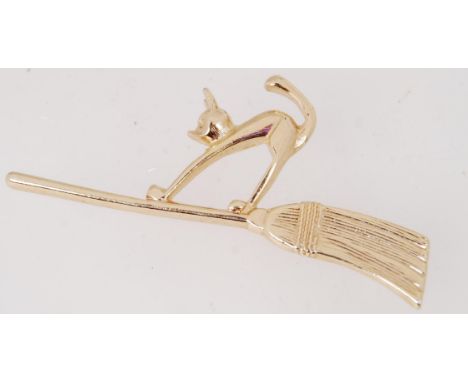 A gold tone metal vintage brooch of a cat on a broom stick. Contains a roll over catch. 6.5cm.