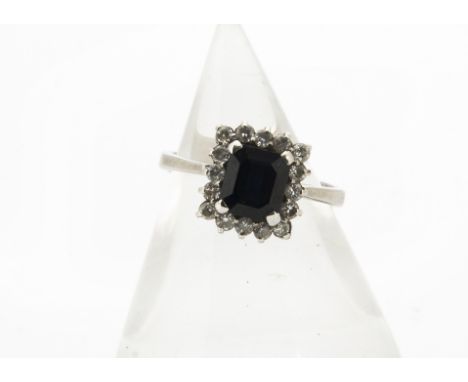 A contemporary sapphire and diamond square cluster ring, the step cut sapphire in four claw setting surrounded by brilliant c