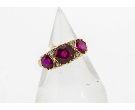 An Edwardian 18ct three stone ruby and diamond chip ring, the central mixed cut ruby, a synthetic replacement, flanked by two