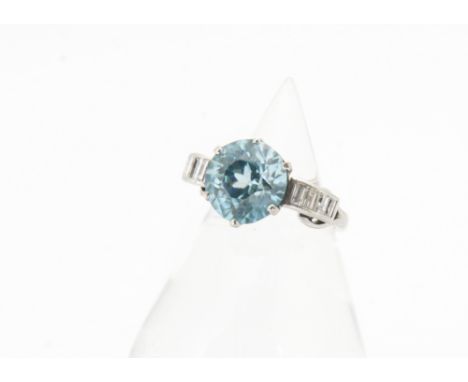 An art deco zircon and diamond dress ring, the circular mixed cut blue zircon in six claw setting flanked by raised baguette 