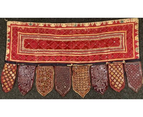 An Indian Toran door hanging, embellished with shisha mirrors and phulkari embroidery, 134cm wide, 72cm drop, late 19th/early