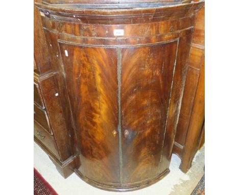 A 19th Century mahogany bow fronted corner cupboard, the pair of doors opening to reveal shelving