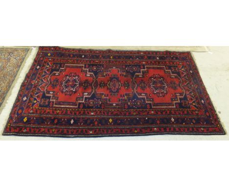 A Persian carpet with repeating medallions on a red ground within a blue and red banded floral decorated border, 289 x 156cm