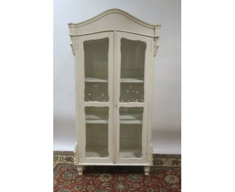 A CONTINENTAL STYLE WHITE PAINTED DISPLAY CABINET the moulded top above a deep frieze with a pair of bevelled glazed doors re