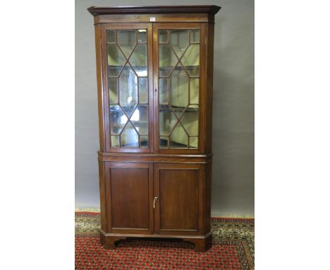 A GEORGIAN STYLE MAHOGANY CORNER CABINET the moulded corners above a plain frieze the pair of astragal glazed doors revealing